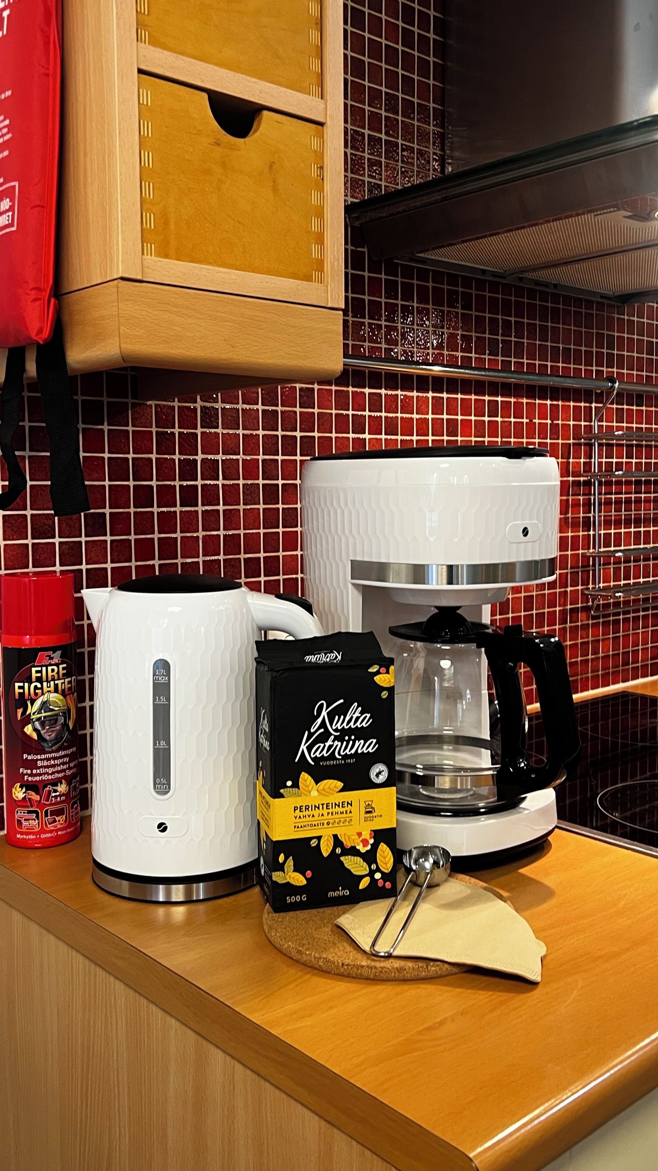 A kitchen counter with a coffee maker, a kettle, a bag of coffee pods, and a fire extinguisher.
