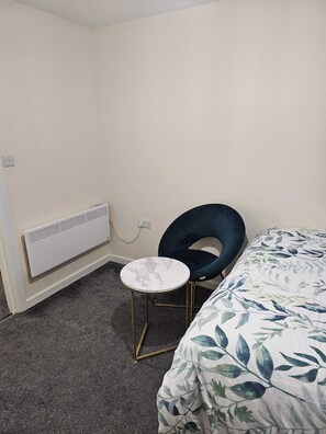 Ein kleines, schlichtes Zimmer mit einem Einzelbett, einem runden Tisch und einem Stuhl.
