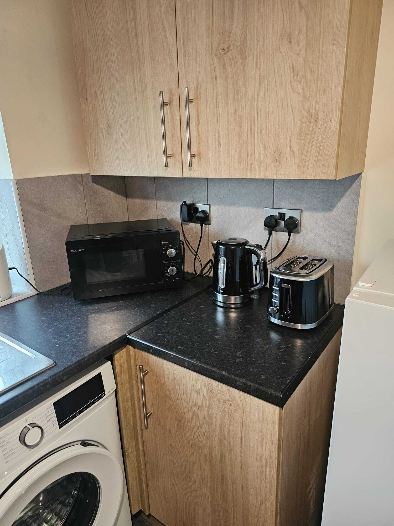Cocina compacta con microondas, hervidor, tostadora y lavadora.