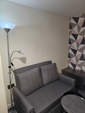 Ein modernes Wohnzimmer mit einem grauen Sofa, einer Stehlampe und einer Wand mit geometrischen Mustern.