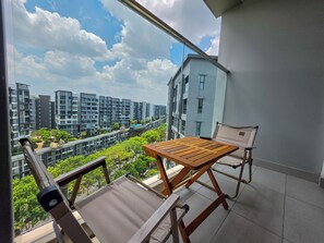 Ein Balkon mit Holztisch und zwei Stühlen, mit Blick auf ein Wohngebiet mit modernen Gebäuden und Grünflächen.