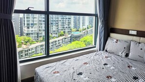 Ett hotellrum med ett stort fönster, en säng med randigt sänglinne och utsikt över höga byggnader.