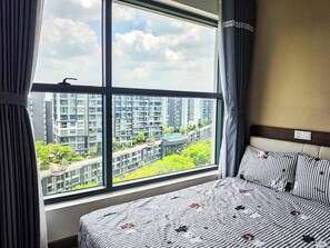 Ein Hotelzimmer mit großem Fenster, einem Bett mit gestreifter Bettwäsche und Blick auf hohe Gebäude.