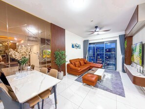 A modern living room with a dining area, a sofa, a coffee table, and a TV. - Luxury 3BR at Diamond Alnata Pool & Gym - Next to Aeon Mall, Park & SGN (Tân Phú)