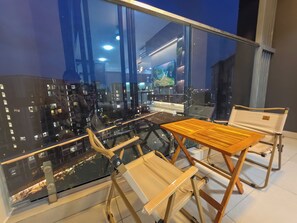 A balcony with a glass railing, a wooden table, and a cushioned chair. - Luxury 3BR at Diamond Alnata Pool & Gym - Next to Aeon Mall, Park & SGN (Tân Phú)
