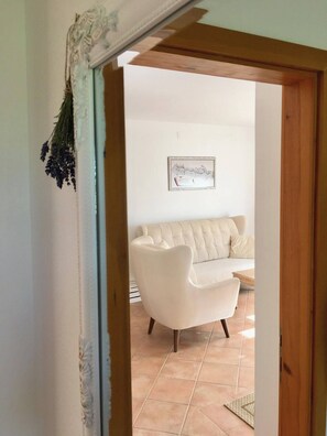 Une porte qui donne sur un salon, où l’on aperçoit un canapé blanc et un tableau encadré accroché au mur.