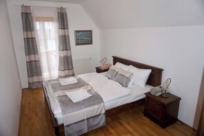 Une chambre à coucher avec un lit, deux tables de chevet, une commode, une fenêtre avec des rideaux et un tableau encadré au mur.