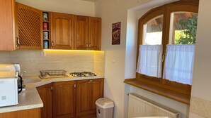Una cocina compacta con armarios de madera, cocina a gas, cafetera y ventana con cortina blanca.