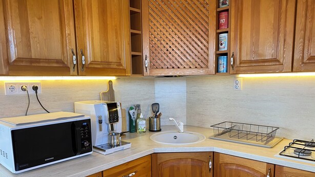 Una cocina con gabinetes de madera, microondas, cafetera y un lavabo.