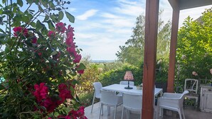 Un patio al aire libre con una mesa y sillas, rodeado de vegetación y vistas al mar.