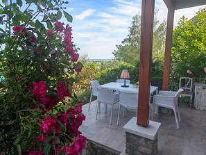 Eine Terrasse im Freien mit Tisch und Stühlen, umgeben von Grünpflanzen und Blick auf das Meer.
