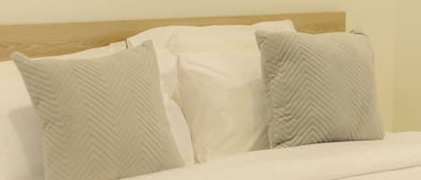 Una cama bien tendida con sábanas blancas y dos almohadas con estampado en zigzag.