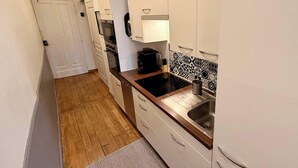 Et smalt køkken med hvide skabe, en sort bordplade og et mønstret backsplash.