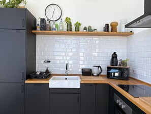 Eine moderne Küche mit weiß gefliestem Spritzschutz, schwarzen Schränken, einer Holz Arbeitsplatte, einem Spülbecken, einer Kaffeemaschine und einer Uhr an der Wand.