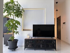 Ein modernes Wohnzimmer mit Flachbildfernseher auf einer Holzkonsolen, einer großen Kühlpflanze und einem schlichten Wanddesign.
