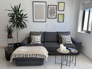 Ein modernes Wohnzimmer mit grauem Sofa, passenden Kissen, einem kleinen Beistelltisch mit Kerzen und einer großen Topfpflanze.