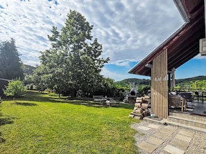 Ein Garten mit einer Terrassenfläche, einem großen Baum und einem Grill.
