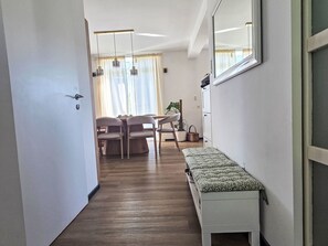 Ein Flur mit einer Bank, ein Essbereich mit Stühlen und einem Tisch sowie ein großer Spiegel an der Wand.