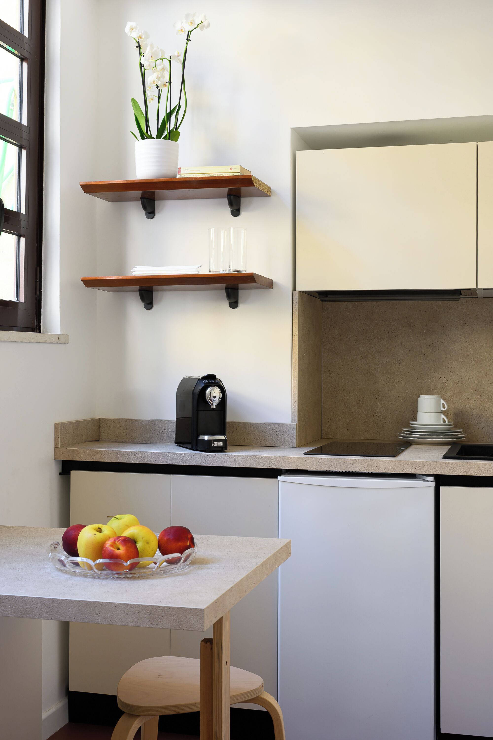 Una cocina compacta con encimera, cafetera, frutero y una orquídea en maceta.