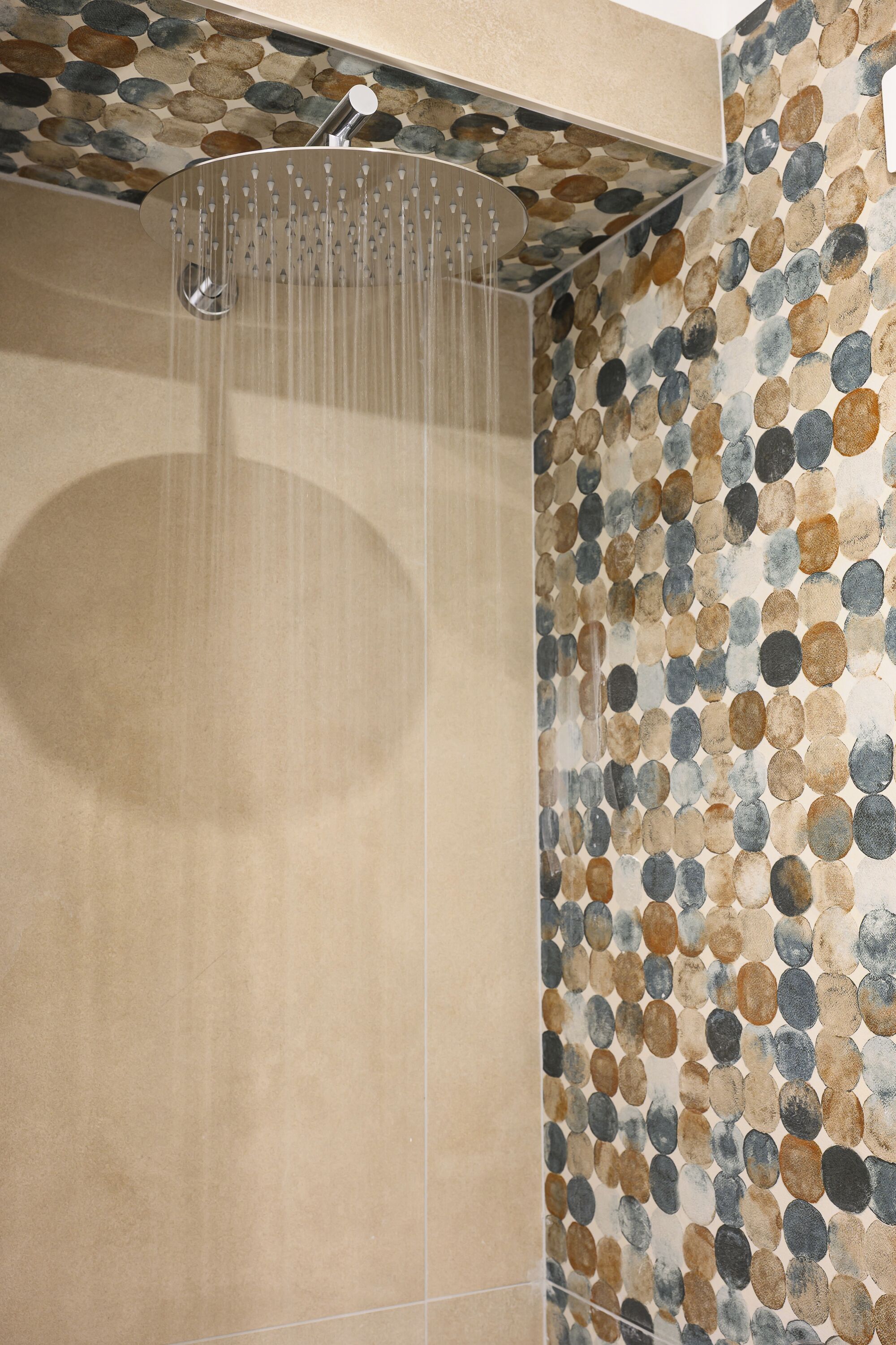 Une douche dotée d’un pommeau de douche créant un effet de pluie et d’un mur orné d’un motif de galets.