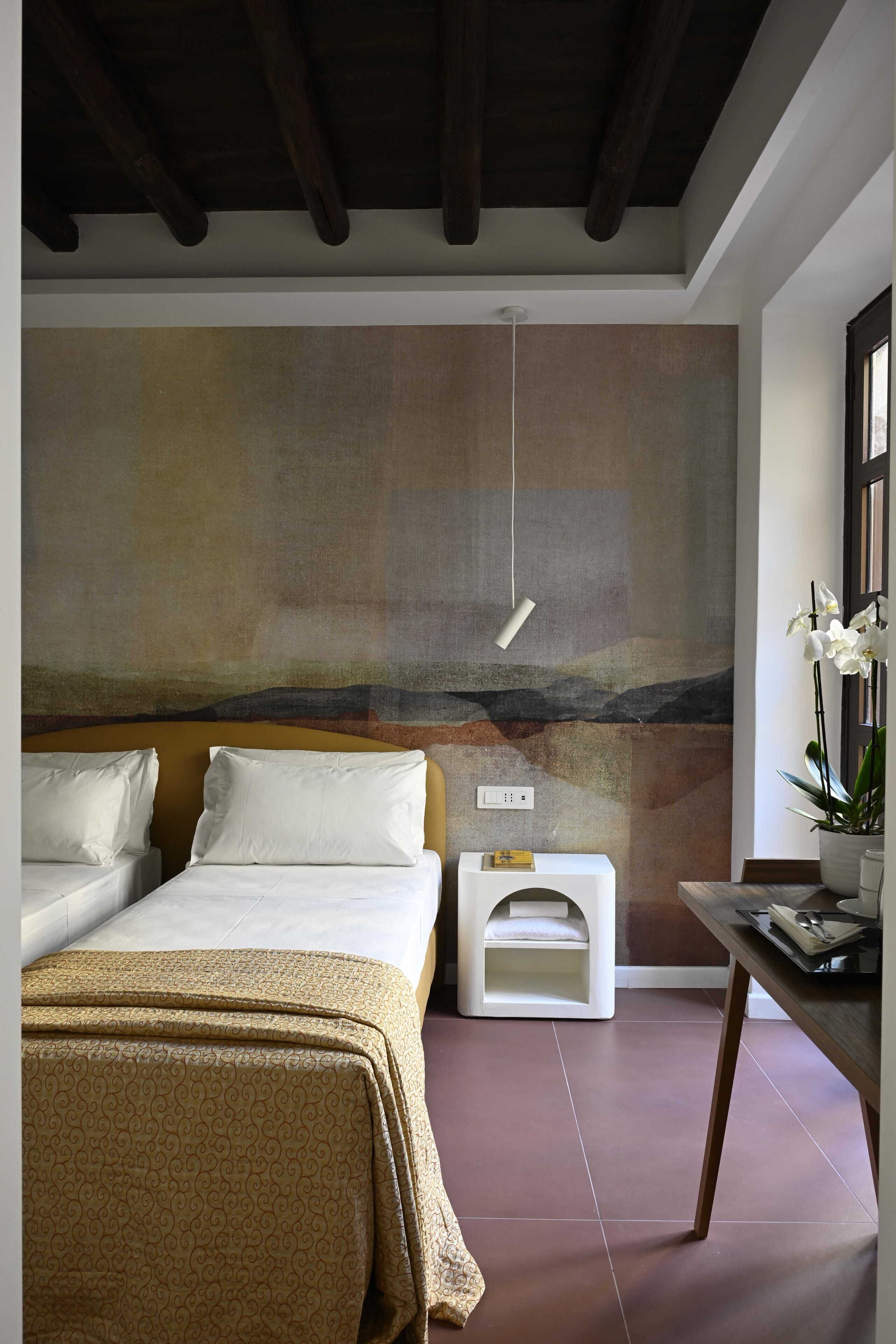 A bedroom with a large bed, bedside tables, a nightstand, and a wall-mounted light fixture.