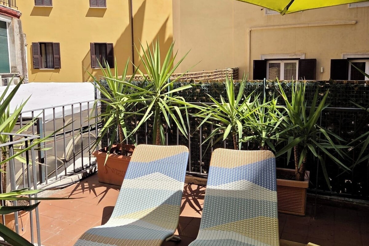 A terrace with two lounge chairs, a yellow umbrella, and potted plants.