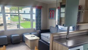 Eine moderne Küche mit Geschirrspüler, ein Essbereich mit Tisch und Stühlen sowie eine Sitzecke mit Sofa und Poufs.