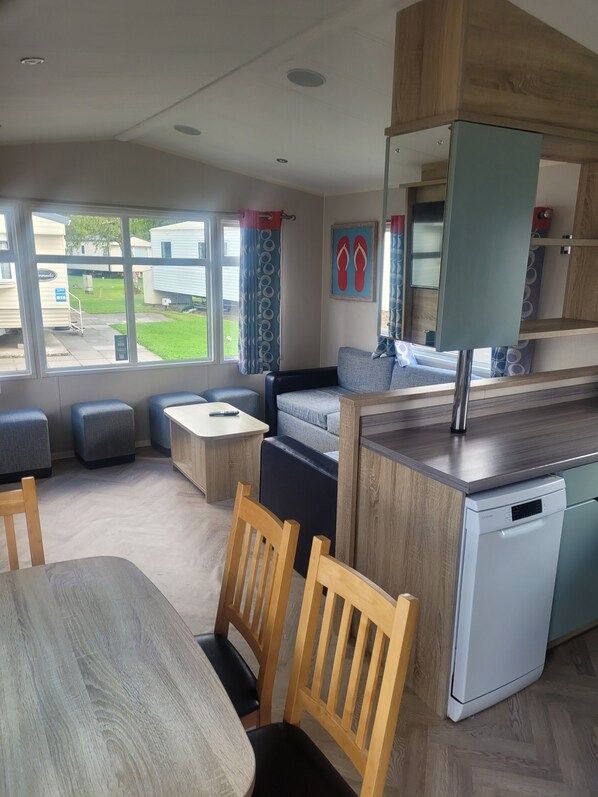 A modern kitchen with a dishwasher, a dining area with a table and chairs, and a seating area with a sofa and ottomans. - Beautiful Caravan minutes from Cartmel & Grange-over-Sands, Lakes are nearby. (Flookburgh)