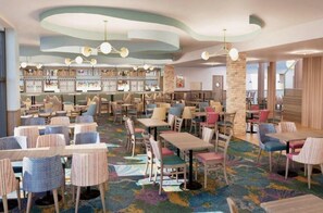 Een ruim restaurant met meerdere tafels en stoelen, een bar en een kleurrijk tapijt.