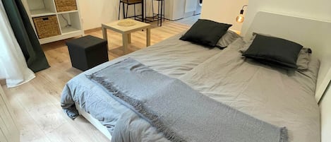 Un dormitorio moderno con una cama grande, una mesita pequeña y un televisor montado en un estante.