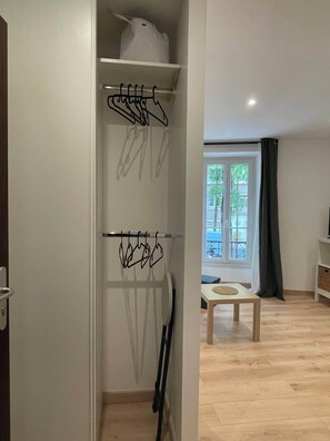 A room with a wooden floor, a white door, a white shelf with a white appliance, a window with a view of greenery, and a small table with a round mat. - Comfortable and quiet studio in the heart of the 15th, easy access to all of Paris (paris)