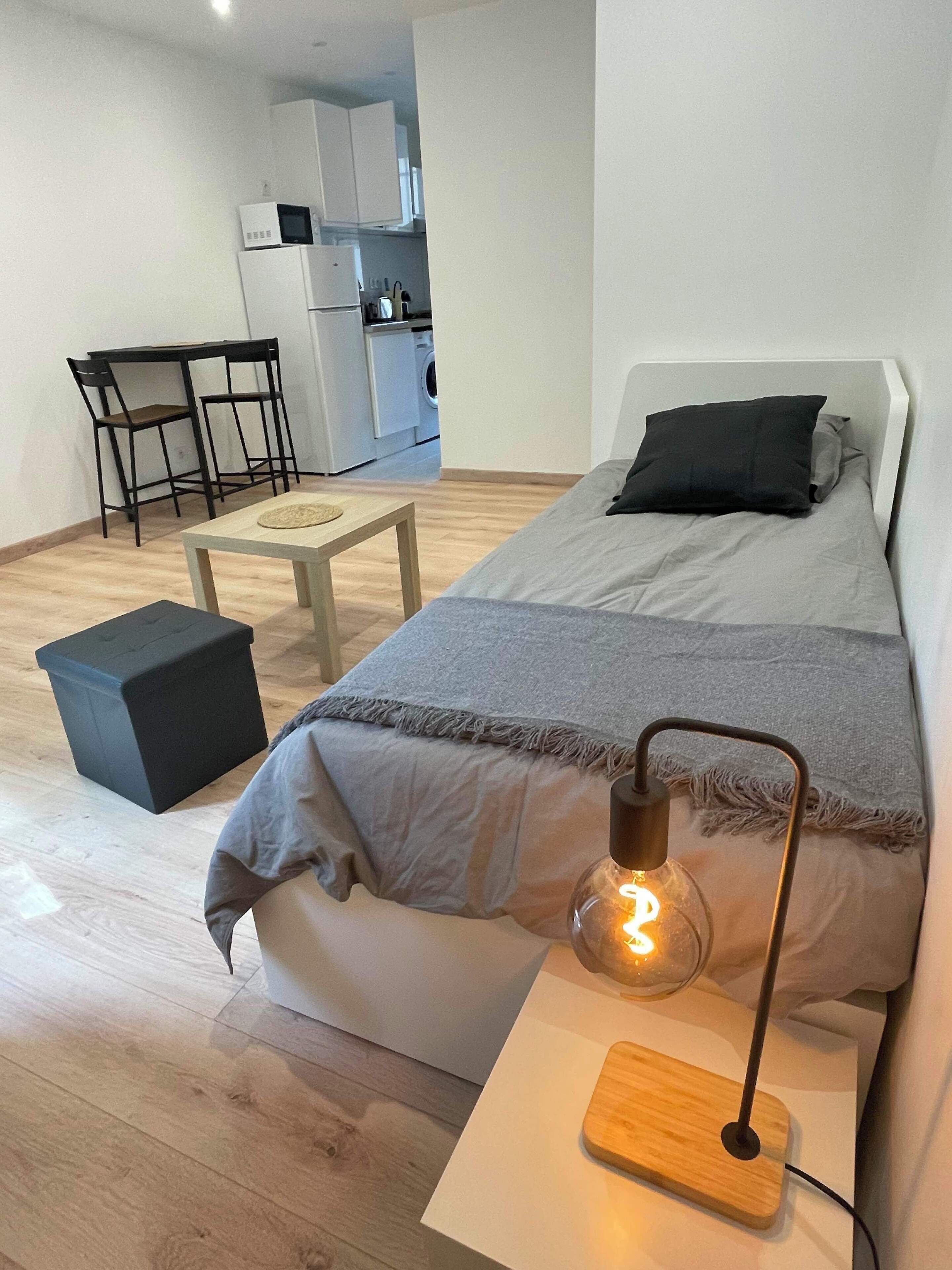 Un dormitorio con cama, mesita de noche, lámpara y una pequeña mesa con sillas.