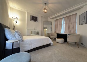 A bedroom with a bed, two chairs, a bedside table, a dresser, a mirror, and a window with curtains. - Luxury Pad for couples next to Paddington station (London)