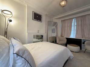 A hotel room with a large bed, bedside tables, a desk, chairs, a mirror, and a window with curtains. - Luxury Pad for couples next to Paddington station (London)