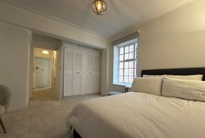 Une chambre à coucher avec un grand lit, une fenêtre, un placard et une porte donnant sur une autre pièce.