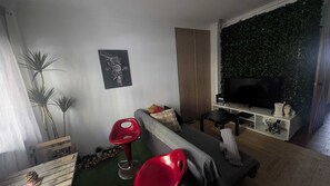 A living room with a sofa, a red chair, a television, and a wall with vertical blinds. - Room charm - Caparica (Costa de Caparica)