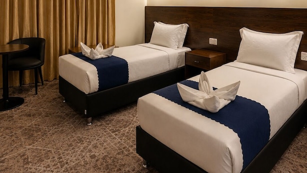 A hotel room with two beds, a desk, and artwork on the walls. - OSCCON Al TAYSEER (Makkah)