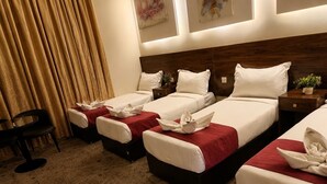 A hotel room with three beds, a desk, and a chair. - OSCCON Al TAYSEER (Makkah)