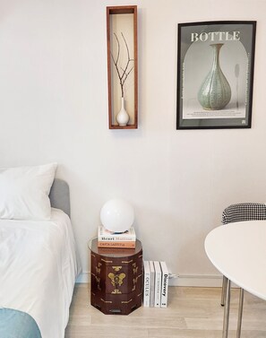 Ein Schlafzimmer mit einem Bett, einem Nachttisch mit Büchern, einer wandmontierten Vase und einem gerahmten Bild.