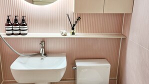 Et badeværelse med et rundt spejl, en vask, et toilet og en hylde med toiletartikler.