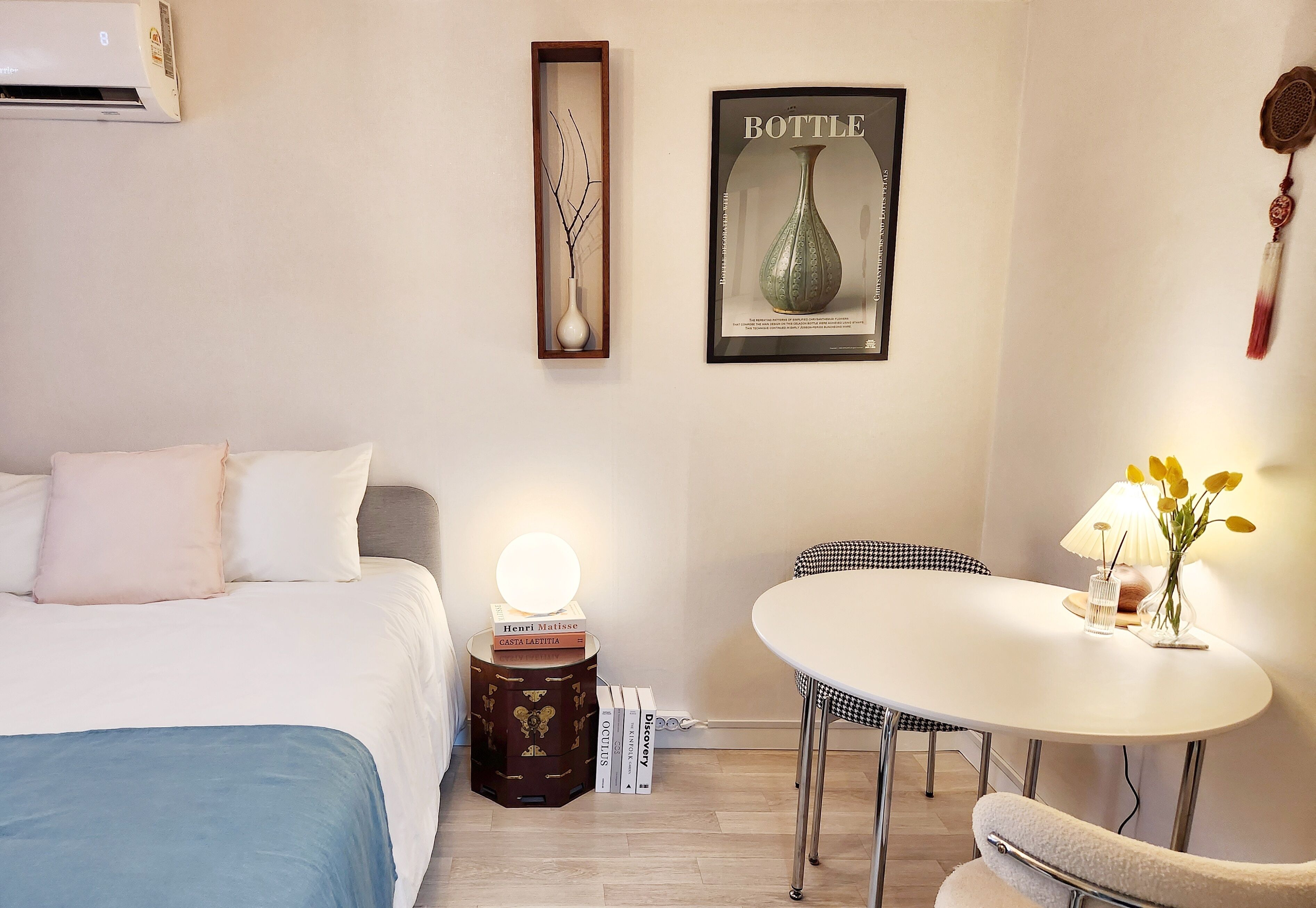 Une chambre d’hôtel comprenant un lit, une table de chevet avec une lampe, une œuvre d’art encadrée, une petite table avec une chaise et un élément décoratif suspendu.