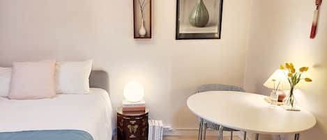 Une chambre d’hôtel comprenant un lit, une table de chevet avec une lampe, une œuvre d’art encadrée, une petite table avec une chaise et un élément décoratif suspendu.