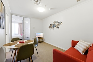Ein modernes Zimmer mit Esstisch, Stühlen, einem Fernseher und einem roten Sofa.
