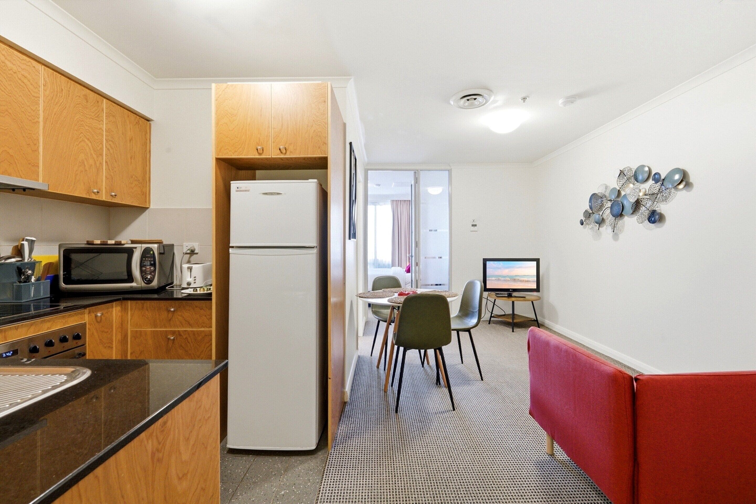 A compact kitchen with modern appliances, a dining area with a TV, and a red cushioned bench.