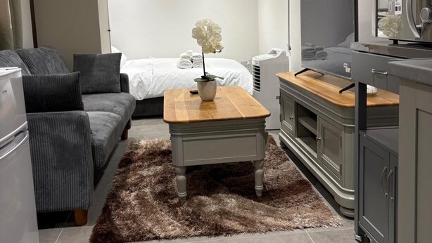 A modern living room with a sofa, a coffee table with a plant, a television, and a cabinet. - Guesthouse Sleeps 2 With Parking (Bootle)