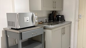 A kitchenette with a microwave, toaster, and coffee maker on a cart, a sink, and cabinets. - Guesthouse Sleeps 2 With Parking (Bootle)