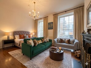 Ein helles Wohnzimmer mit einem grünen Sofa, einem grauen Sofa, einem Kamin und einer Deckenleuchte.