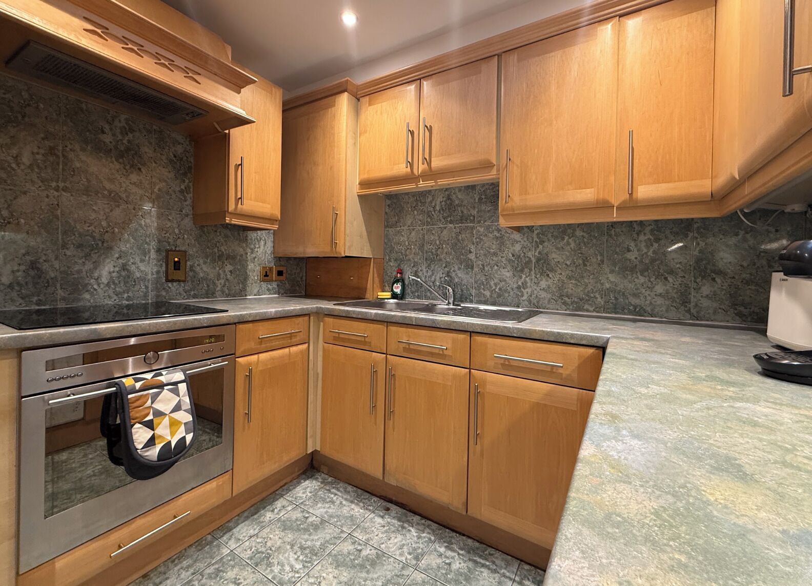 Eine Küche mit Holzschränken, einem eingebauten Ofen und einer Arbeitsplatte aus Granit.
