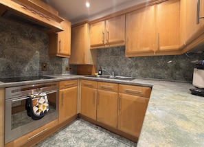 Eine Küche mit Holzschränken, einem eingebauten Ofen und einer Arbeitsplatte aus Granit.