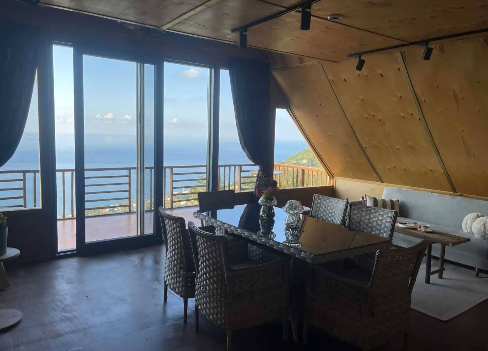 Uma sala de jantar com vista para o oceano, grandes janelas e teto de madeira.